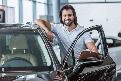 portrait of smiling man standing at new car in dealership salon