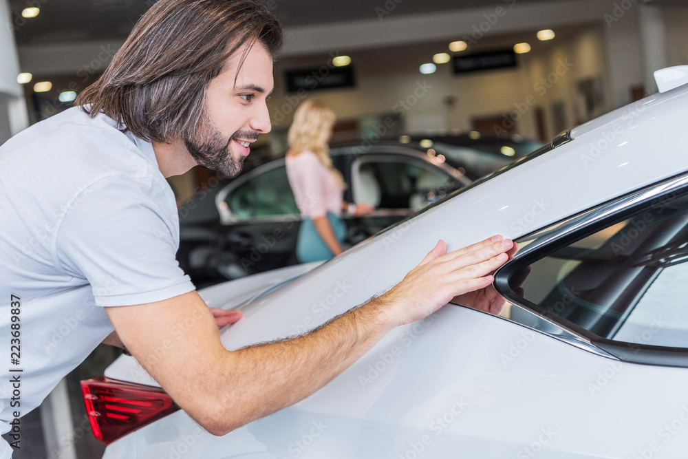 selective focus of man checking automobile with girlfriend on background at dealership salon