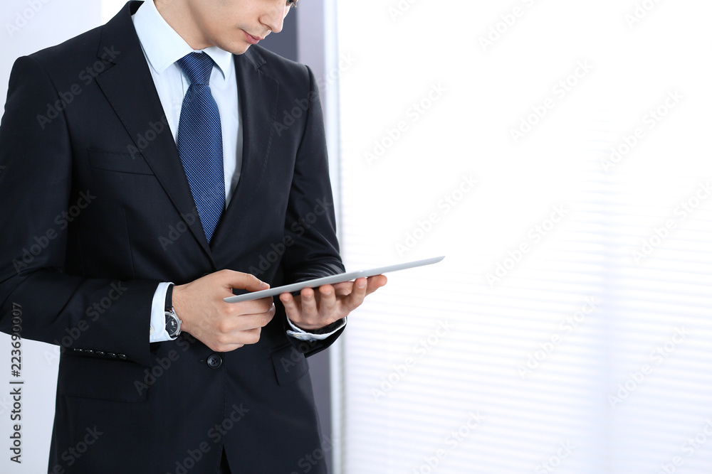 Young businessman using tablet computer while standing straight in office. Business concept Young businessman using tablet computer while standing straight in office. Business concept