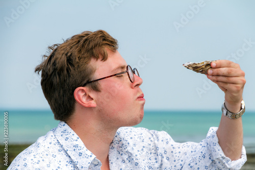 Young man enjoys the taste of fresh raw oysters at the french coast of Brittany (Bretagne) in Cancale, France on a summer day
