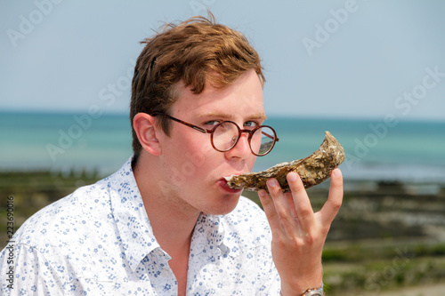 Young man enjoys the taste of fresh raw oysters at the french coast of Brittany (Bretagne) in Cancale, France on a summer day