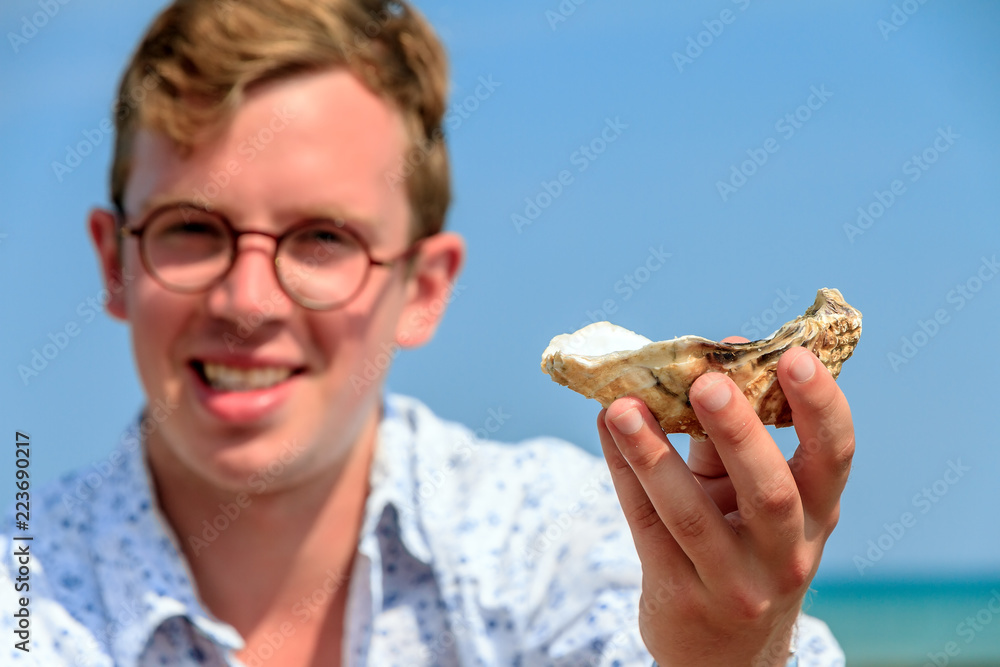 Young man shows a fresh raw oysters at the french coast of Brittany (Bretagne) in Cancale, France on a summer day Young man shows a fresh raw oysters at the french coast of Brittany (Bretagne) in Cancale, France on a summer day