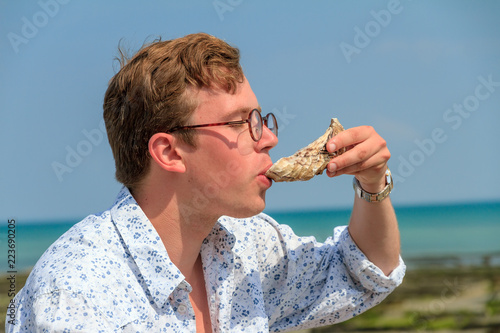 Young man enjoys the taste of fresh raw oysters at the french coast of Brittany (Bretagne) in Cancale, France on a summer day
