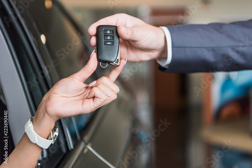 cropped shot of dealership salon seller giving car key to woman in auto salon