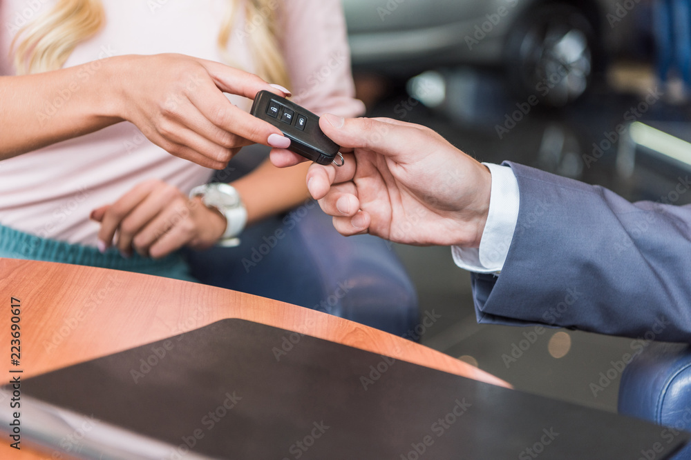 cropped shot of dealership salon seller giving car key to woman in auto salon