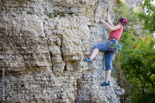 Photo of side view of young athlete woman in red helmet climbing up mountain