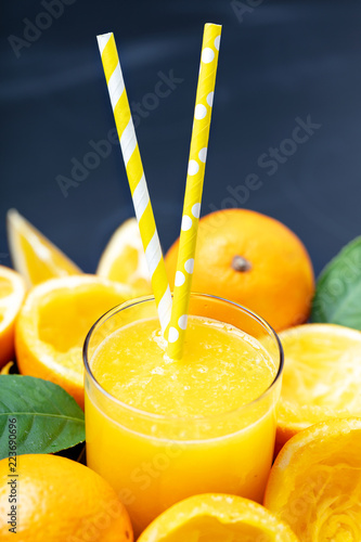 Glass of orange juice surrounded by orange squeezed halves and whole fruits , vertical comosition photo