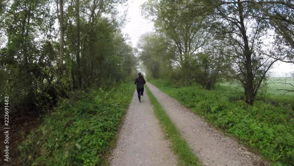 Following a woman running on a gravel road through the countryside on a foggy morning Following a woman running on a gravel road through the countryside on a foggy morning