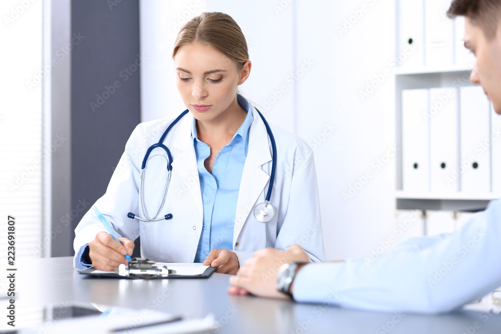 Doctor and patient in hospital. Beautiful blonde physician consulting business man about his health. Medicine concept Doctor and patient in hospital. Beautiful blonde physician consulting business man about his health. Medicine concept