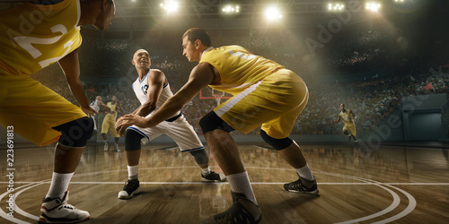 Basketball players on big professional arena during the game. Tense moment of the game. Male caucasian and black players fight for the ball