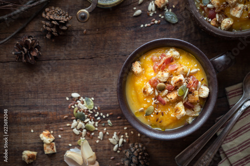 Traditional Thanksgiving homemade pumpkin or squash soup garnished with bacon, croutons and seeds. Overhead view