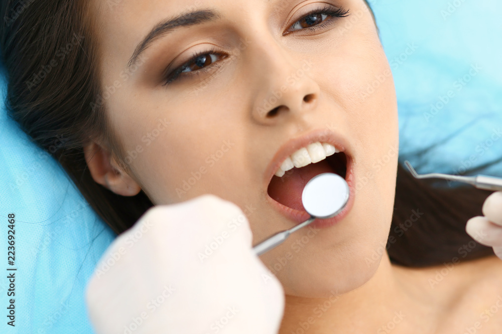 Young female patient visiting dentist office.Beautiful woman with healthy straight white teeth sitting at dental chair with open mouth during oral checkup while doctor working at teeth Young female patient visiting dentist office.Beautiful woman with healthy straight white teeth sitting at dental chair with open mouth during oral checkup while doctor working at teeth