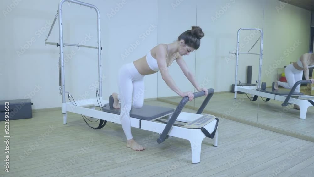 Pilates. Woman in white clothes practicing stretching exercise on reformer in gym. all series by number 01234567890001. Pilates. Woman in white clothes practicing stretching exercise on reformer in gym. all series by number 01234567890001.