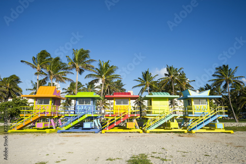Row of brightly painted colorful lifeguard towers with coconut palm trees on Miami Beach promenade.
