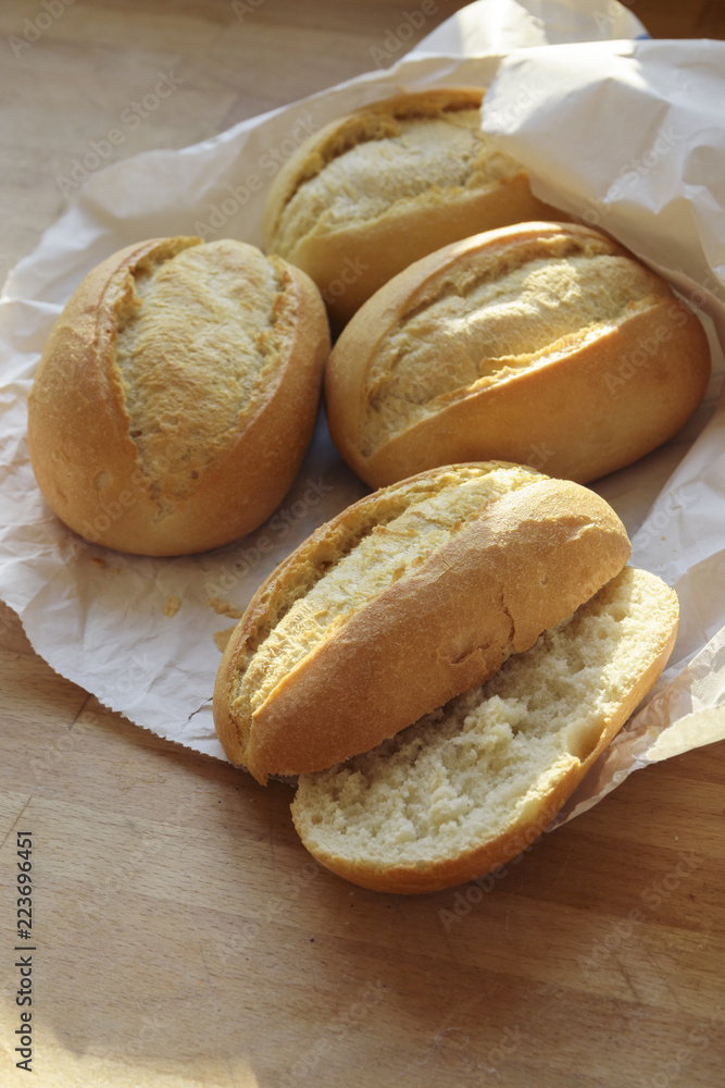 bread rolls or buns whole and halved fresh from the bakery in a white paper bag on a wooden table, vertical