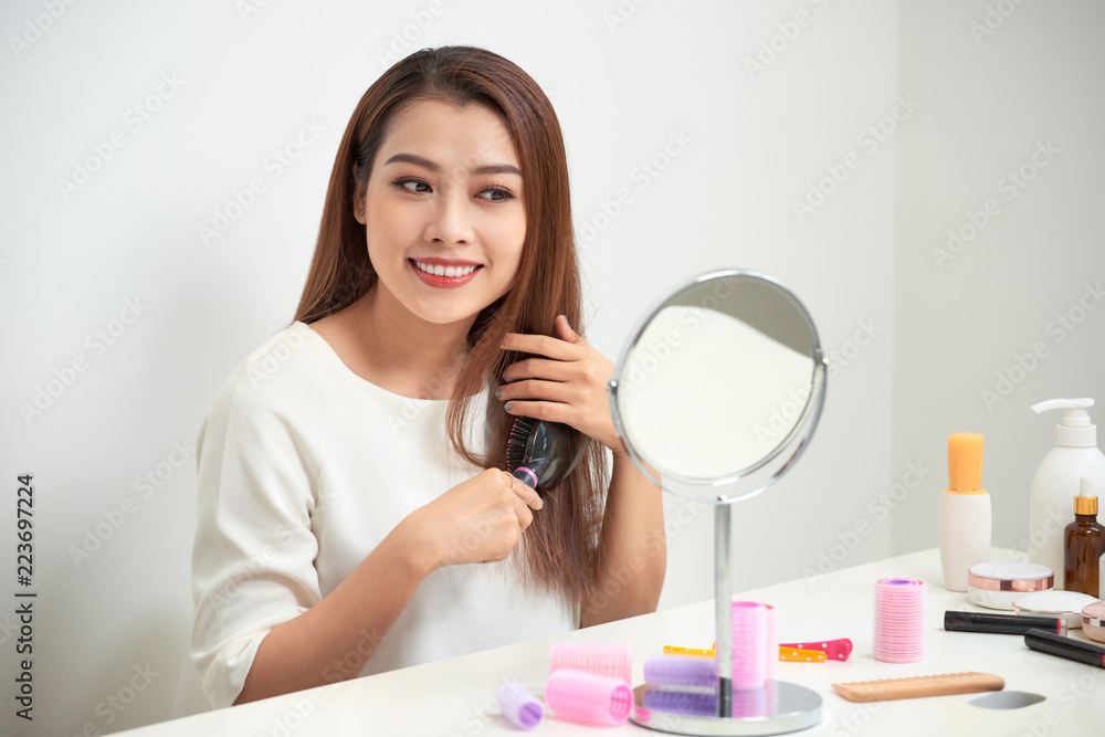 Getting rid of tangles. Beautiful young woman looking at her reflection in mirrorand brushing her long hair while sitting at the dressing table Getting rid of tangles. Beautiful young woman looking at her reflection in mirrorand brushing her long hair while sitting at the dressing table