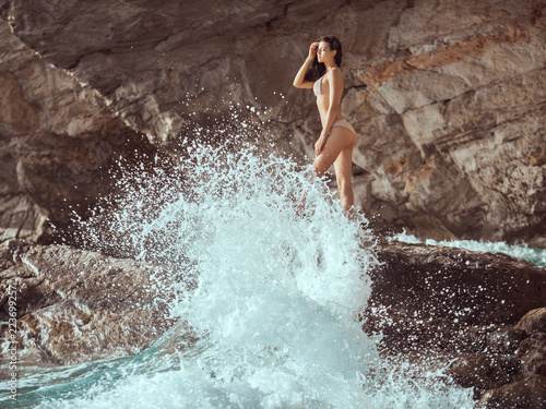 Romantic passion young girl in bikini outdoors against wild tropical sea background. Beautiful sensual brunette mixed race Asian Caucasian woman with slim sporty tanned body standing on rock in water