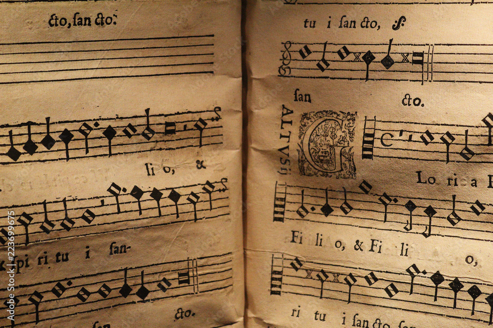 Fototapeta premium An old score written on a parchment, showing a few staves with notes and a miniature, for a song in Latin