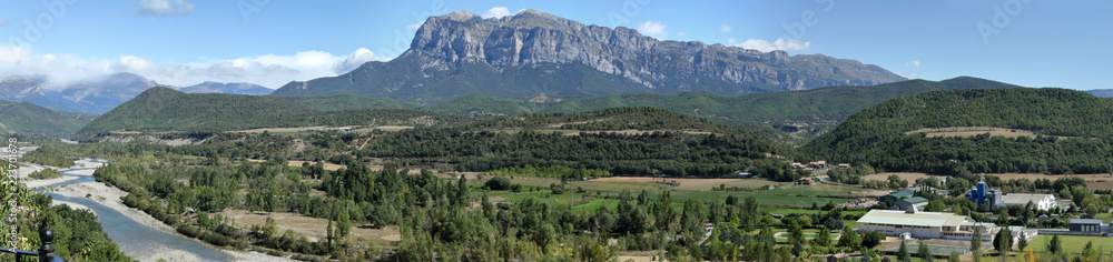A landscape with blue sky, some clouds and the The Peña Montañesa mountain massif in the Spanish Aragonese Pyrenees, as seen from Ainsa, a small, stone made, rural town from the Middle Ages A landscape with blue sky, some clouds and the The Peña Montañesa mountain massif in the Spanish Aragonese Pyrenees, as seen from Ainsa, a small, stone made, rural town from the Middle Ages