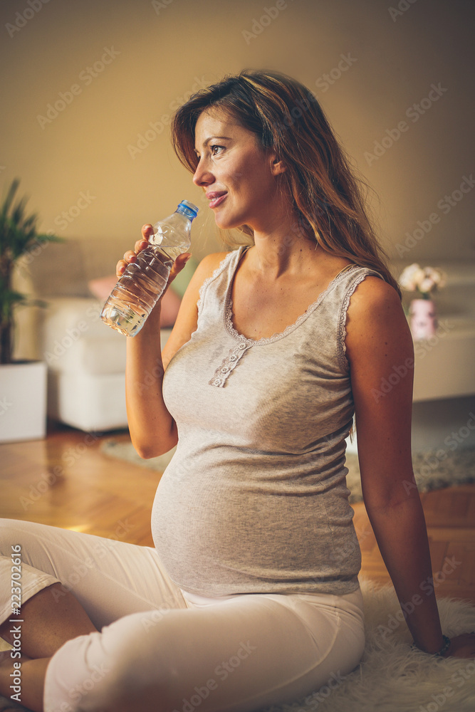 Pregnant woman sitting on floor and drinking water. Pregnant woman sitting on floor and drinking water.