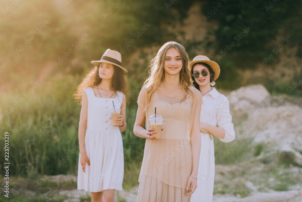 attractive girls in straw hats holding coffee latte and walking in nature with sunlight