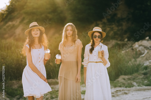 stylish beautiful girls in straw hats holding cups of coffee latte and posing  with sunlight
