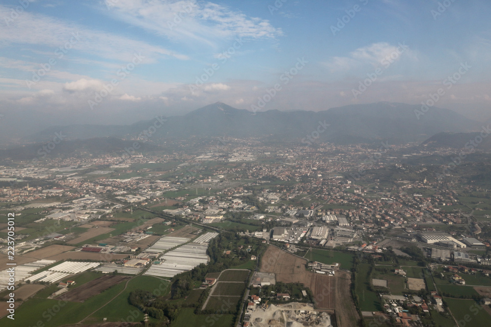 An areal landscape of the Po Valley (Pianura Padana) with forests, mountains, cultivated fields and cities, as seen from an airplane