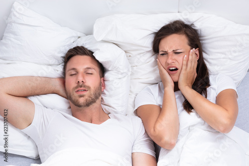 Woman Covering Her Ears While Man Snoring On Bed