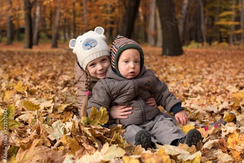 Dzieci zasypane w liściach jesienią w parku. Rodzeństwo.