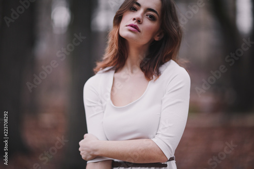 Attractive charming young woman in a white cotton dress and dark coat walking in the autumn park. Cloudy. Soft colors of nature. The melancholy mood.