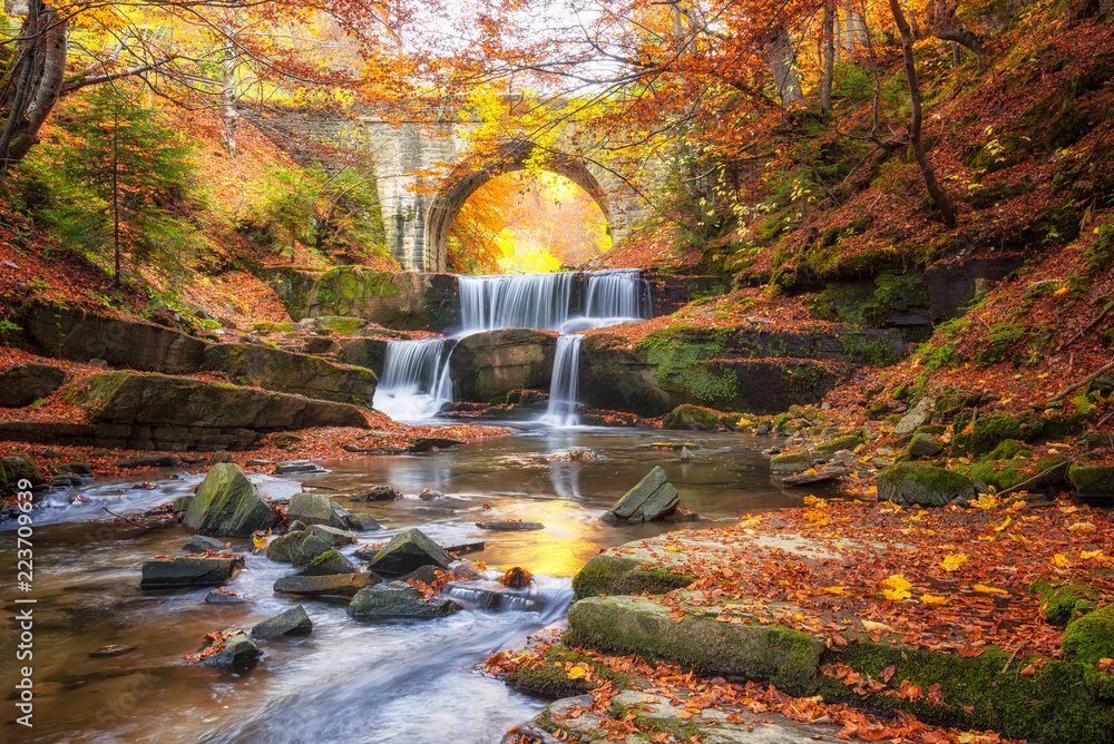 Fototapeta premium Jesień bajki przez rzekę / jesień rzeki z pięknymi kaskadami wody i stary most w pobliżu miejscowości Sitovo, Bułgaria