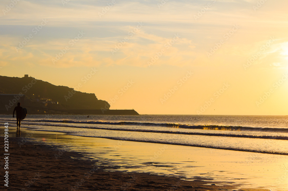 Surfer walking on a beach in Cornwall at sunset