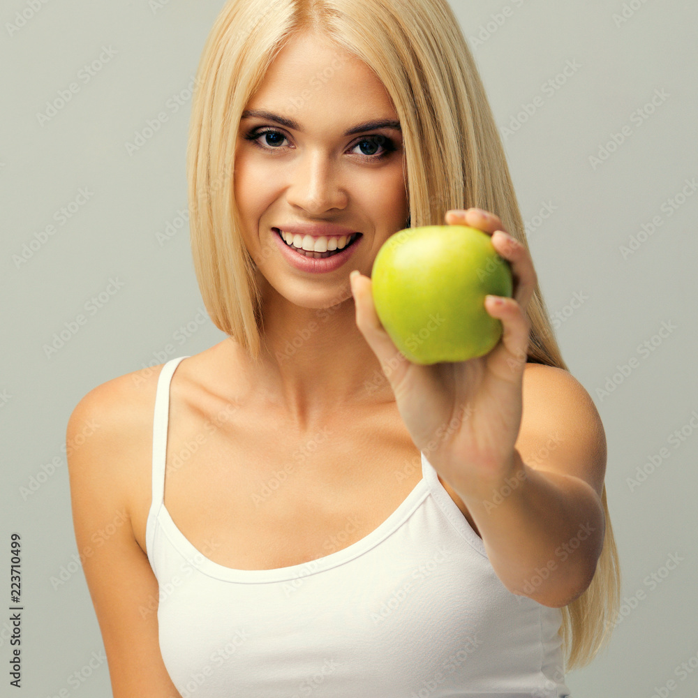 Woman sitting on floor, showing apple, against grey. Woman sitting on floor, showing apple, against grey.