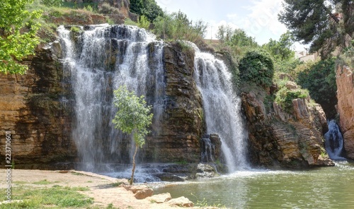A landscape of the the Huerva river rock double waterfalls surrounded by green trees and bushes in the Muel park during spring, Spain