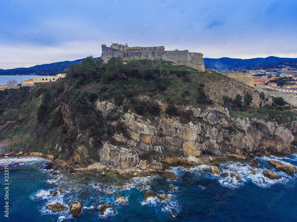 The waves of the Mediterranean sea are broken on a rock on which there is an ancient stone fort