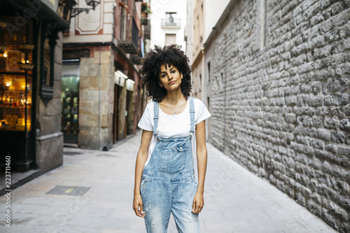 Spain, Barcelona, portrait of woman with curly hair wearing dungarees