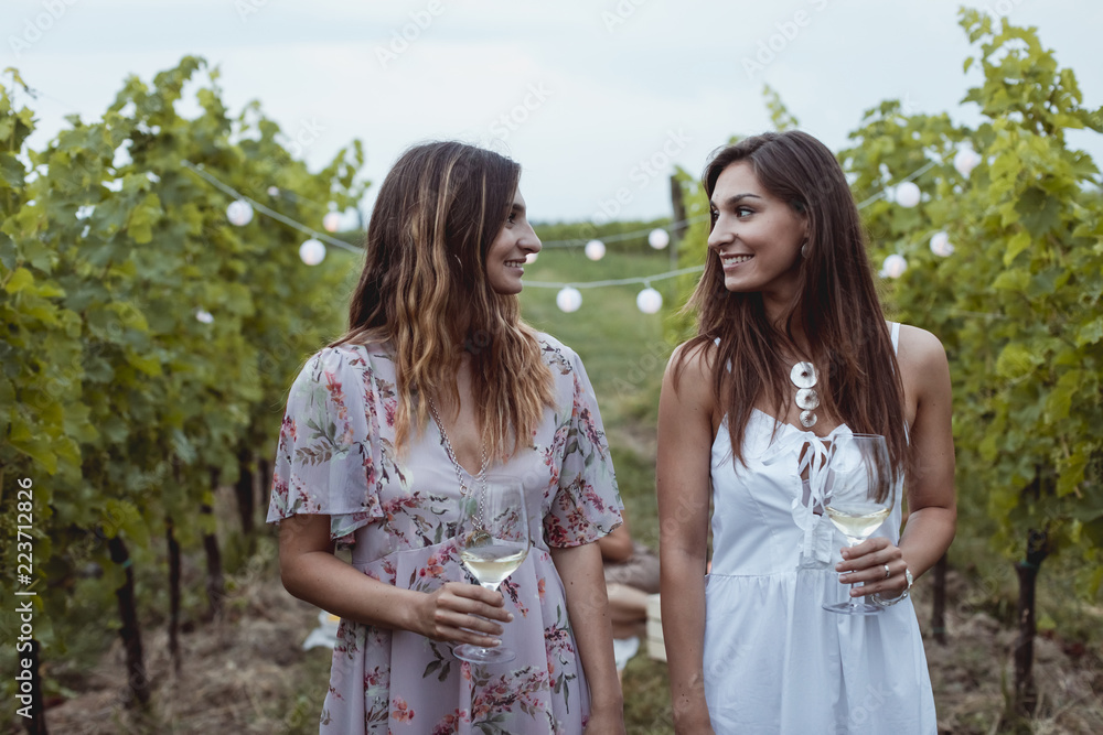 Young female friends with wine glasses walking in vineyard Young female friends with wine glasses walking in vineyard