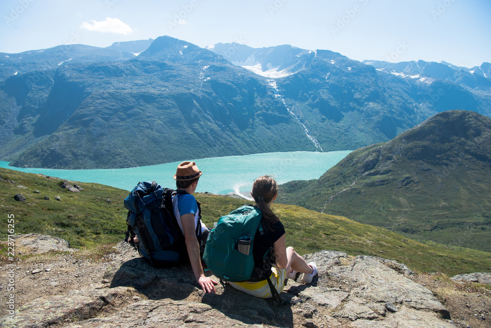 couple of hikers resting and looking at Besseggen ridge over Gjende lake in Jotunheimen National Park, Norway