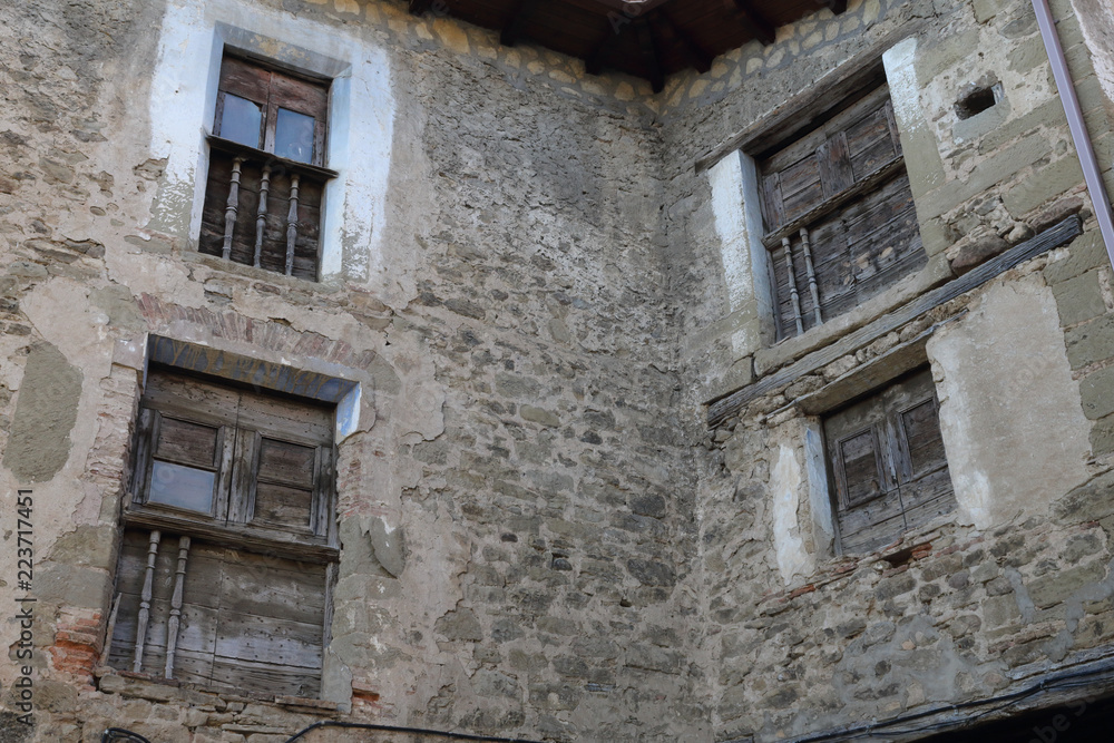 Four smal windows with old shabby wooden shutters and a railing on a stone grey houes in Biel, a small town in Aragon, Spain