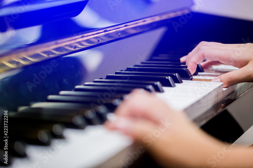 Selective focus to fingers of woman teaching boy to play the piano.