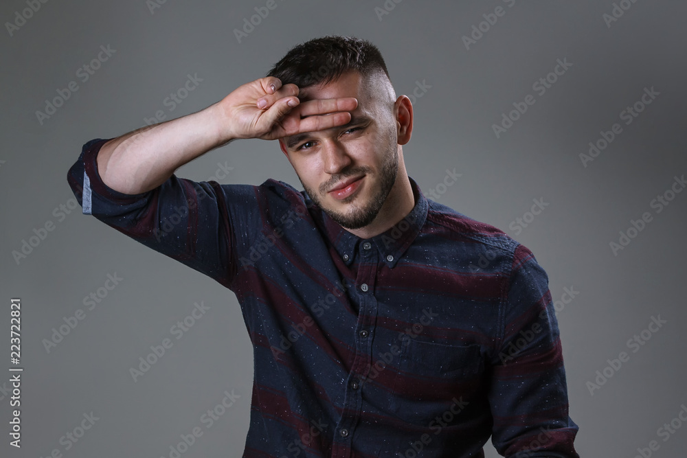 Studio portrait of handsome positive male keeping his two fingers over his eyes. Bearded man looking at the camera keep his fingers on forehead on studio wall background.