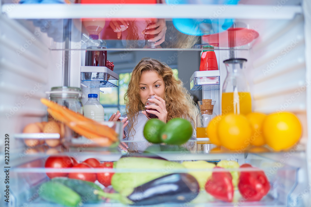 Woman smelling jam in front of fridge full of groceries. Woman smelling jam in front of fridge full of groceries.