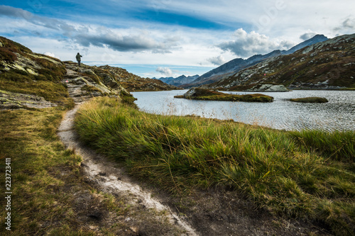 man walking in a mountains trail in switzerland alps with lake and cloudy sky photo