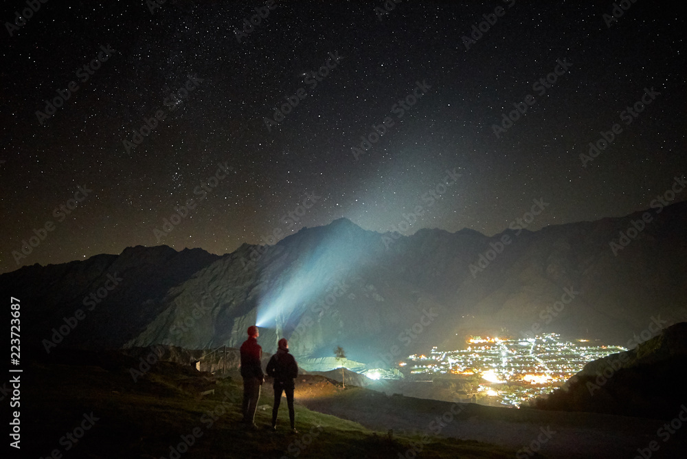 Happy couple hikers under night sky and city lights at background