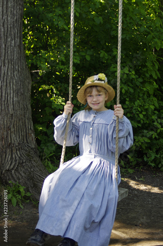 Girl dressed in vintage blue dress on tree swing 