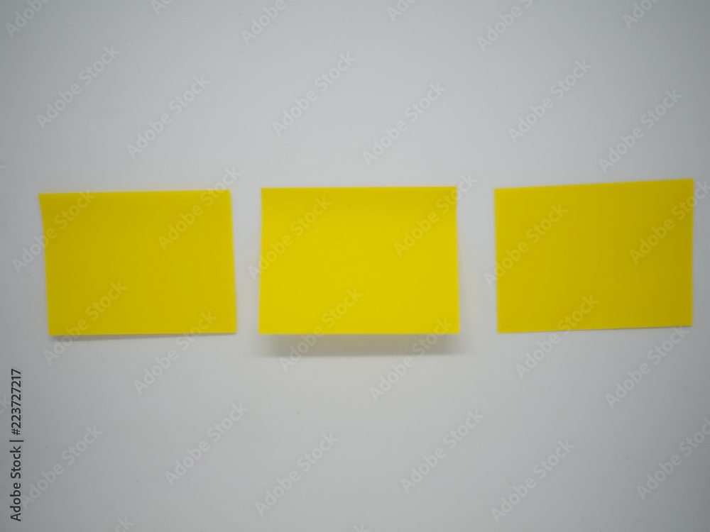 Three yellow sticky note stick horizontally on the white isolated wall Three yellow sticky note stick horizontally on the white isolated wall