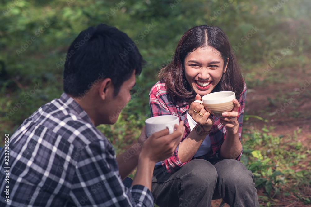 Asian couple sitting and drinking coffee in front of the tent in the camp. Asian couple sitting and drinking coffee in front of the tent in the camp.