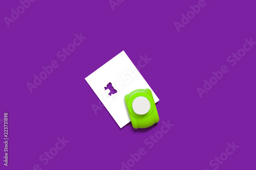 plastic green hole puncher with a sheet of paper in it standing on the purple background. concept of office chancery. free space for text