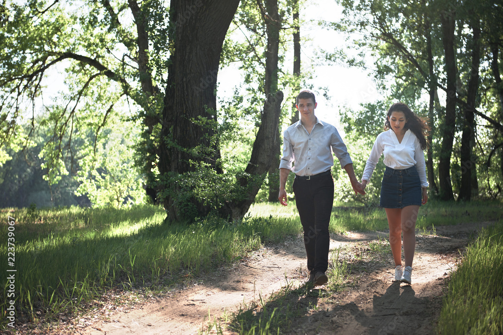 Fototapeta premium young couple walking in the forest, summer nature, bright sunlight, shadows and green leaves, romantic feelings