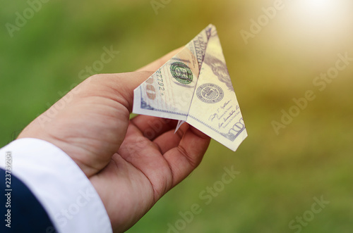 The hands of businessmen are holding dollars folded into an airplane with a bright sky, the concept of competitiveness of business